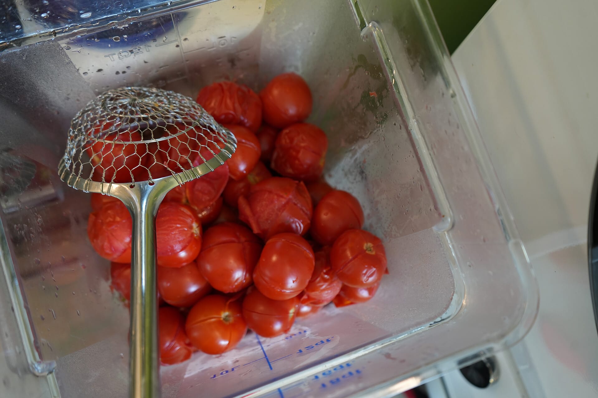 A bin of tomatoes with a spider strainer laying on top