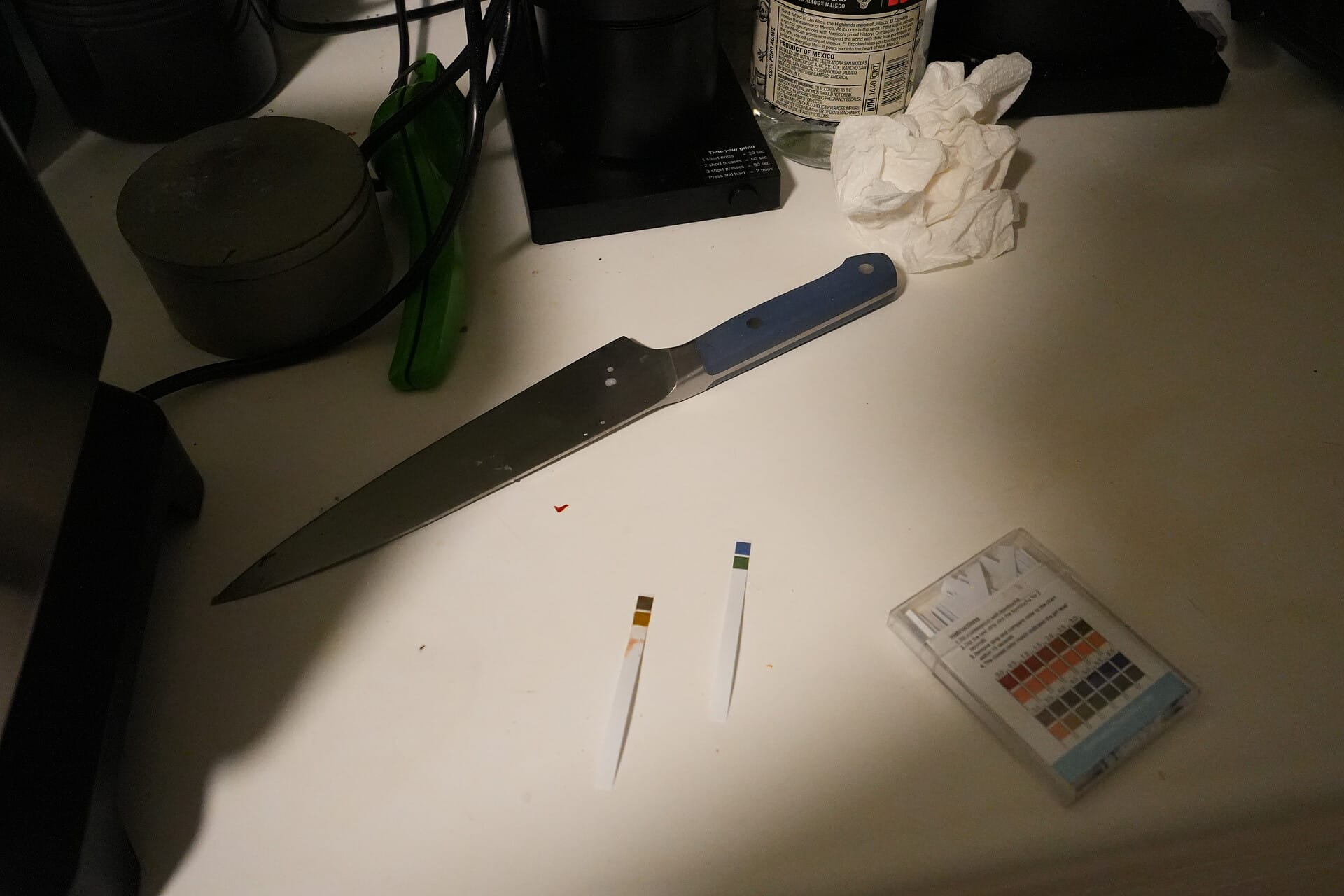 A messy kitchen counter with two pH test strips in the middle. One is used and covered in tomato sauce.