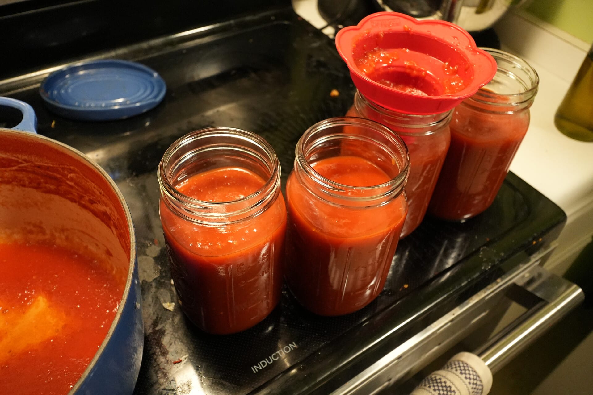 Four quart jars filled with tomato sauce and a nearly empty pot slightly out of frame