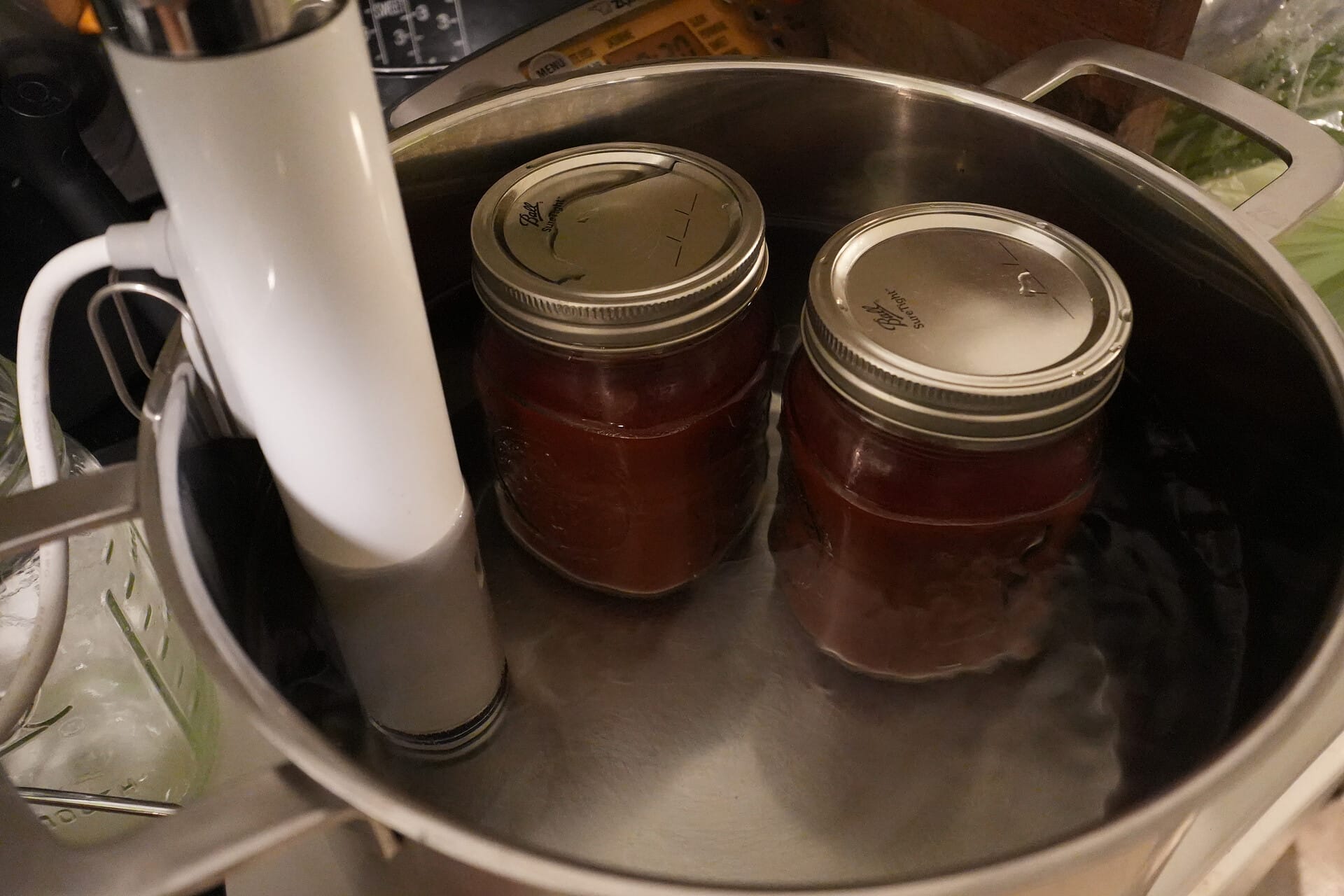 Two jars filled with tomato in a pot filled with water. A Joule circulator is inserted for heating.